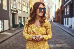 Smiling woman wearing sunglasses exploring city streets with her cellphone Smiling woman wearing sunglasses exploring city streets with her cellphone